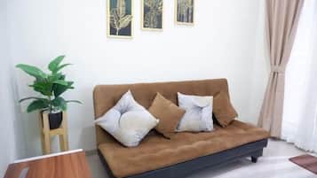 A brown sofa with two pillows, a potted plant, and framed artwork on the wall.