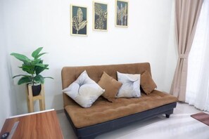 Un sofá marrón con dos almohadas, una planta en maceta y cuadros en la pared.