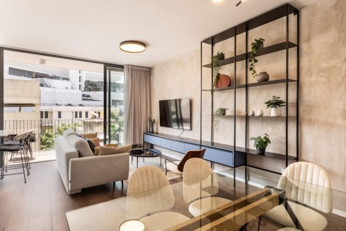 Un salon moderne avec un canapé, des fauteuils, une table à manger en verre, un téléviseur et une étagère pour les plantes.