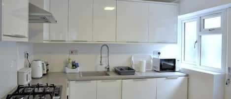 A kitchen with white cabinets, a gas stove, a microwave, and a window.