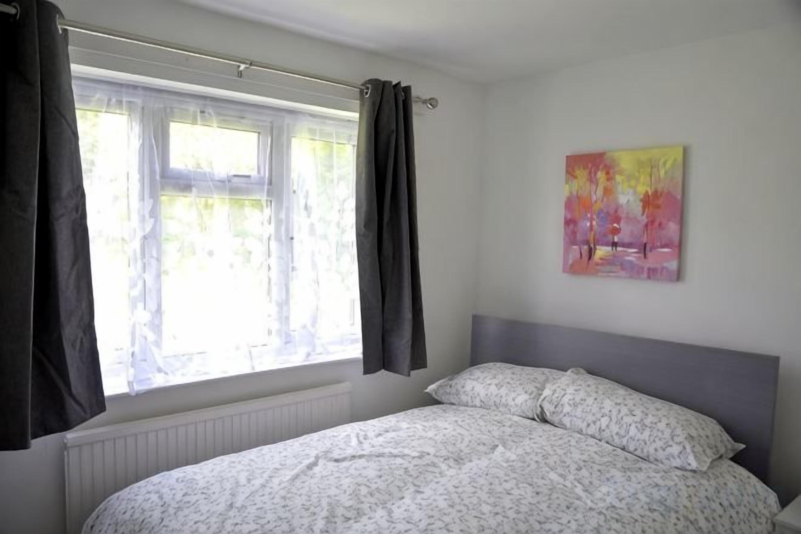 Un dormitorio con una cama, una ventana con cortinas y un cuadro en la pared.