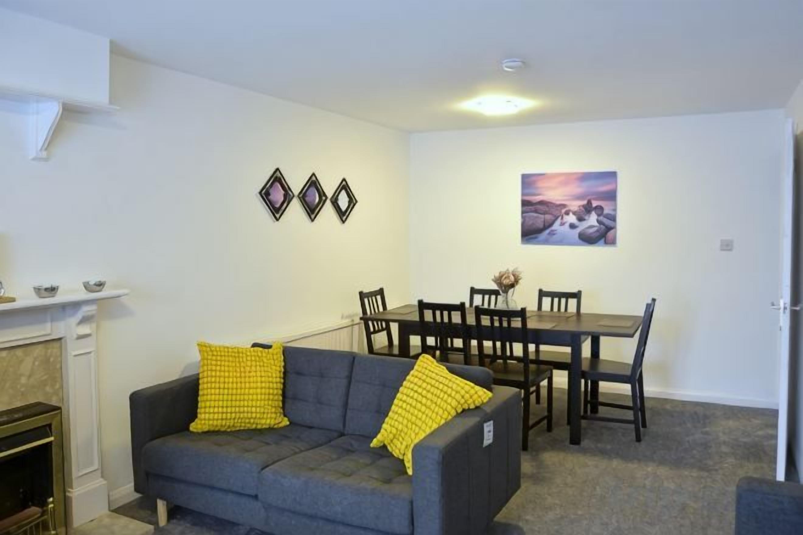 En stue med sofa, spisebord med stole, pejs og billeder på væggen.