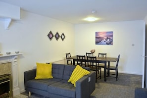 A living room with a sofa, a dining table with chairs, a fireplace, and wall decorations. - Lindrick Villa Peaceful 3Bd Bungalow Parking (Leicester)