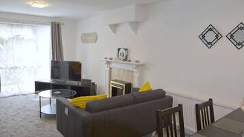 A living room with a sofa, a fireplace, a television, and a dining table.