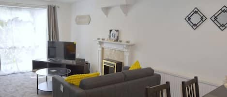 A living room with a sofa, a fireplace, a television, and a dining table.