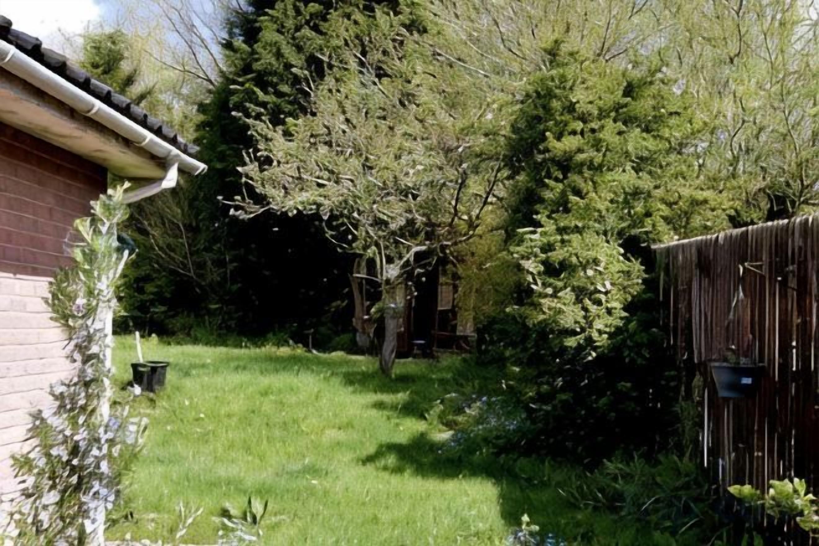 A backyard with a grassy lawn, a wooden fence, and a brick building.
