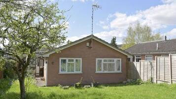 A single-story brick house with a sloped roof, a satellite dish, and a fenced yard.