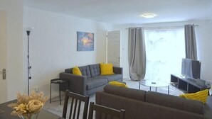 Ein Wohnzimmer mit einer Couch, einem Couchtisch, einem Fernseher und einem Essbereich mit Tisch und Stühlen.