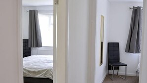 Ein Schlafzimmer mit einem Bett, einem Sessel, einem Fenster mit Vorhängen und einer Tür.
