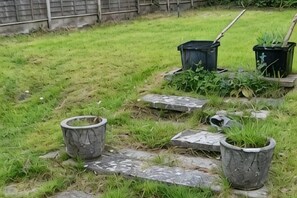 Een tuin met stenen traptreden, potplanten en een hark.
