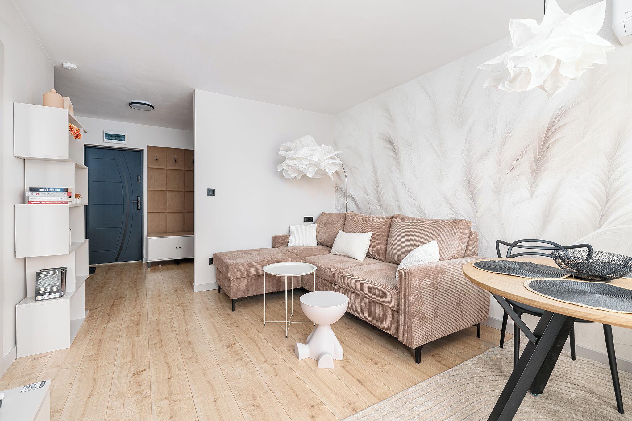 A modern living room with a sectional sofa, a round dining table, and a white decorative wall piece.