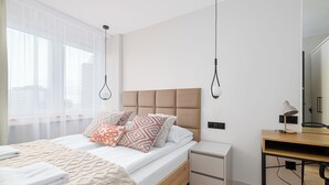 A modern bedroom with a bed, bedside tables, a desk, and a large window. - RentPlanet - Apartament Rondo ONZ (Warsaw)