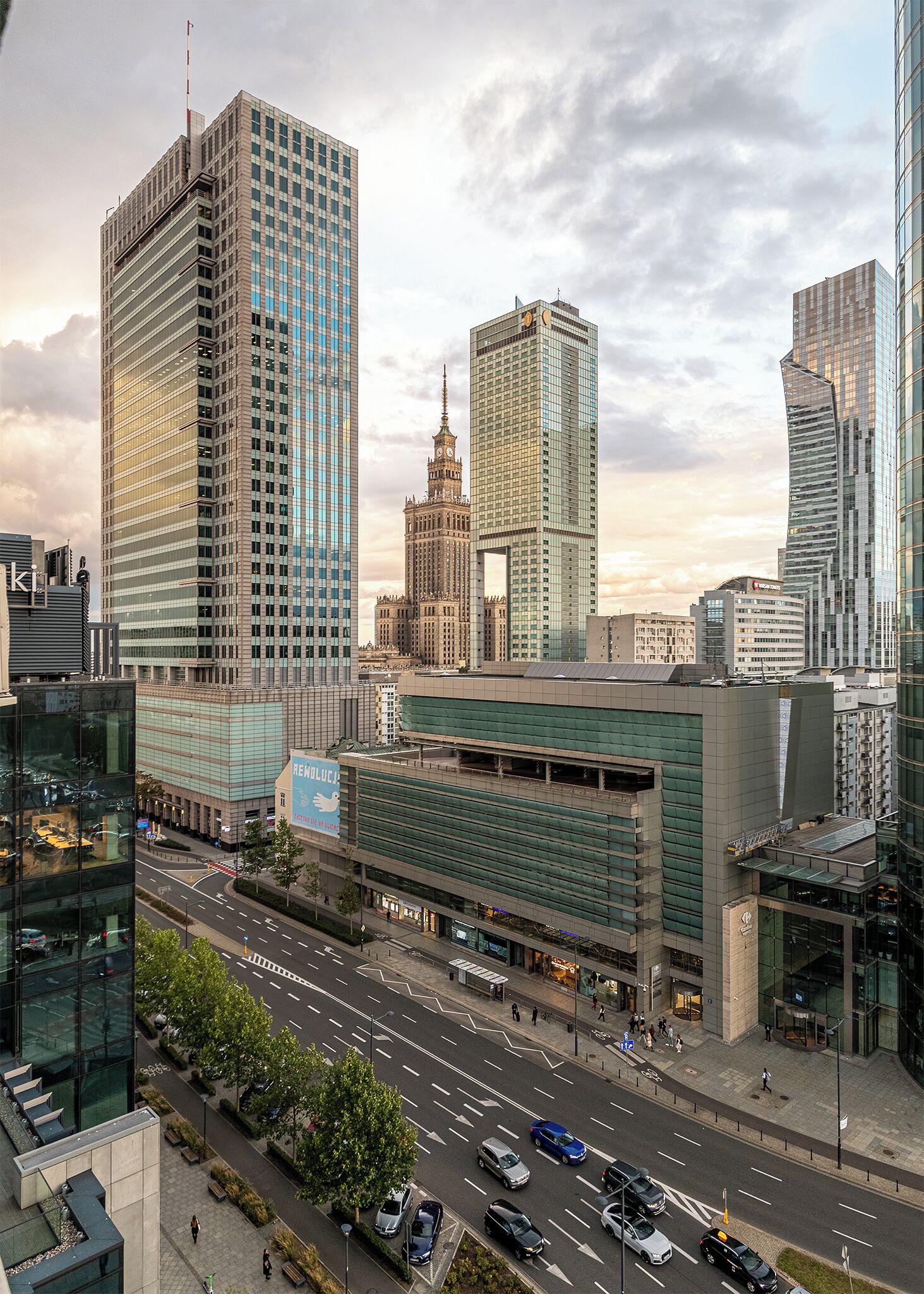 Un paisaje urbano moderno con rascacielos, una imponente torre del reloj y una intersección concurrida.