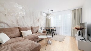 A modern living room with a brown sofa, a small round table, and a flat-screen TV on a stand. - RentPlanet - Apartament Rondo ONZ (Warsaw)