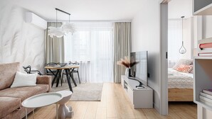 A modern, well-lit living room with a sofa, TV, and dining area. - RentPlanet - Apartament Rondo ONZ (Warsaw)