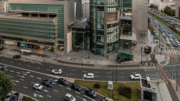 A modern urban area with high-rise buildings, a busy intersection, and a prominent bank building. - RentPlanet - Apartament Rondo ONZ (Warsaw)