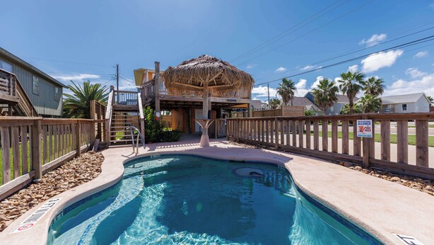Une piscine dotée d’une terrasse en bois, d’une structure surmontée d’un toit de chaume et d’une clôture en bois.