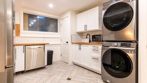 A compact kitchen with a built-in washer and dryer, white cabinetry, and a herringbone-patterned floor. - 2 Bedrooms l  Sleeps 4 Adults l Kitchenette (Fernie)