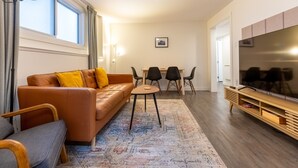 A modern living room with a leather sofa, a coffee table, a TV stand, and a dining area with chairs and a table. - 2 Bedrooms l  Sleeps 4 Adults l Kitchenette (Fernie)
