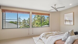 A bedroom with a bed, two windows, a ceiling fan, and a framed picture on the wall.