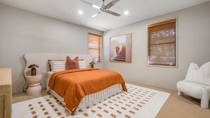 Een slaapkamer met een bed, een stoel, een plafondventilator en twee ramen met jaloezieën.