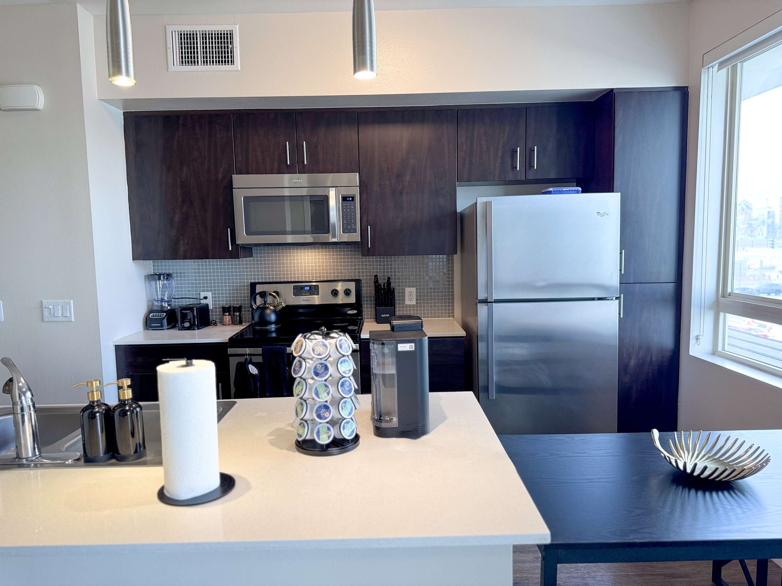 A modern kitchen with dark wood cabinets, stainless steel appliances, and a central island with a coffee machine and a large white candle.