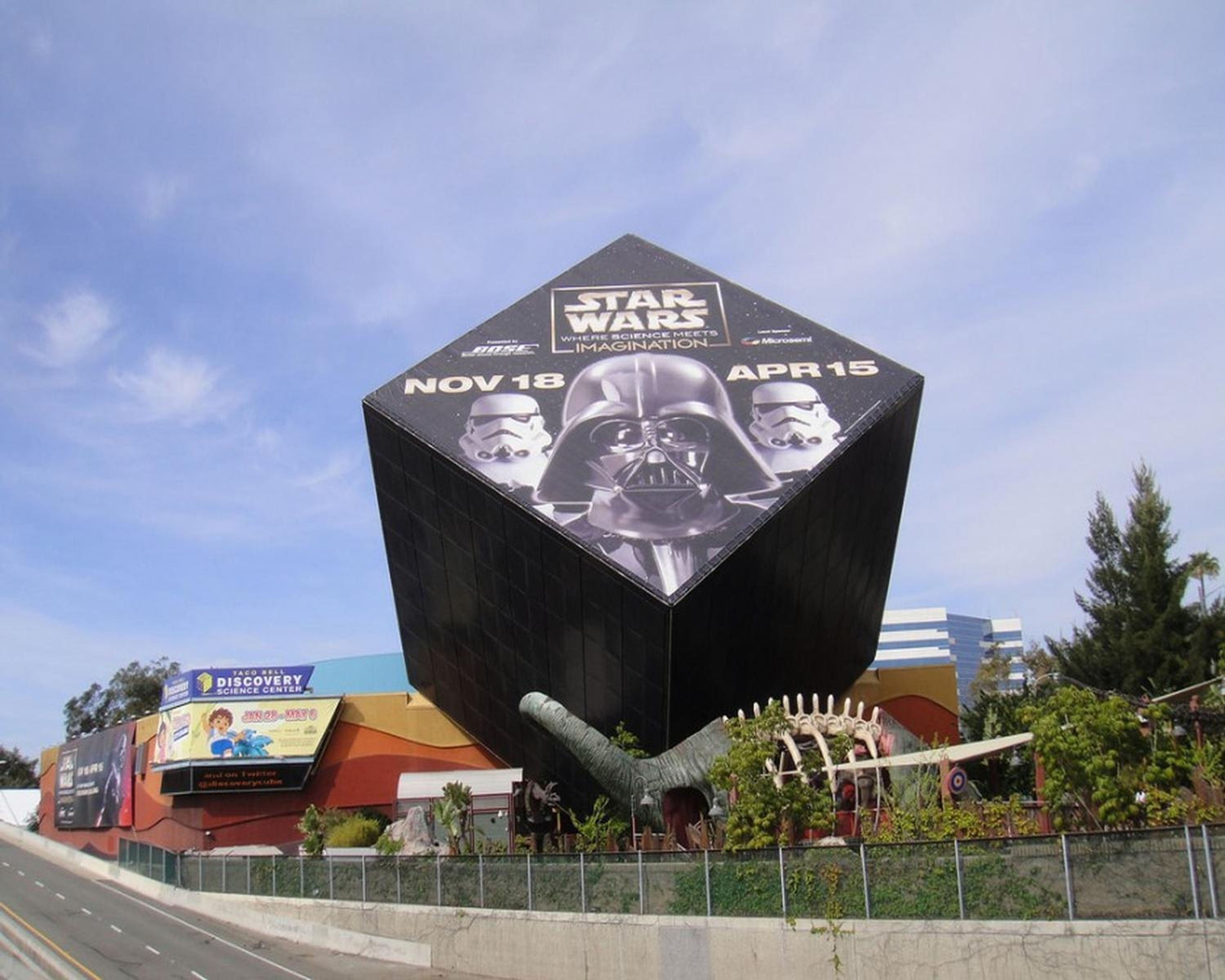 A large Star Wars-themed sculpture with a hexagonal base and a curved top, located in a public area with surrounding greenery and a Taco Bell sign in the background.