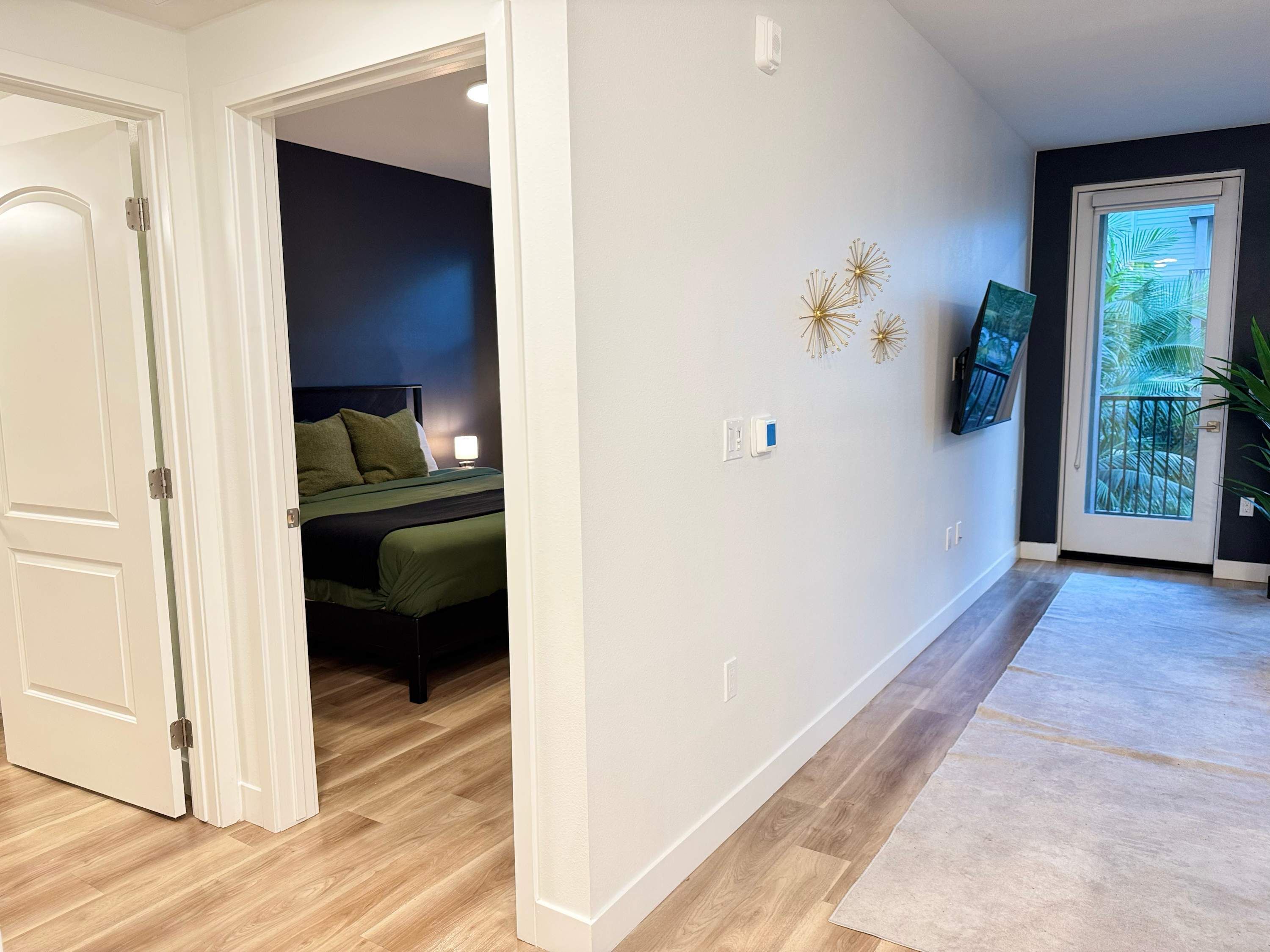 A hotel room with a bed, a nightstand, a lamp, and a view of the outdoors through a door.