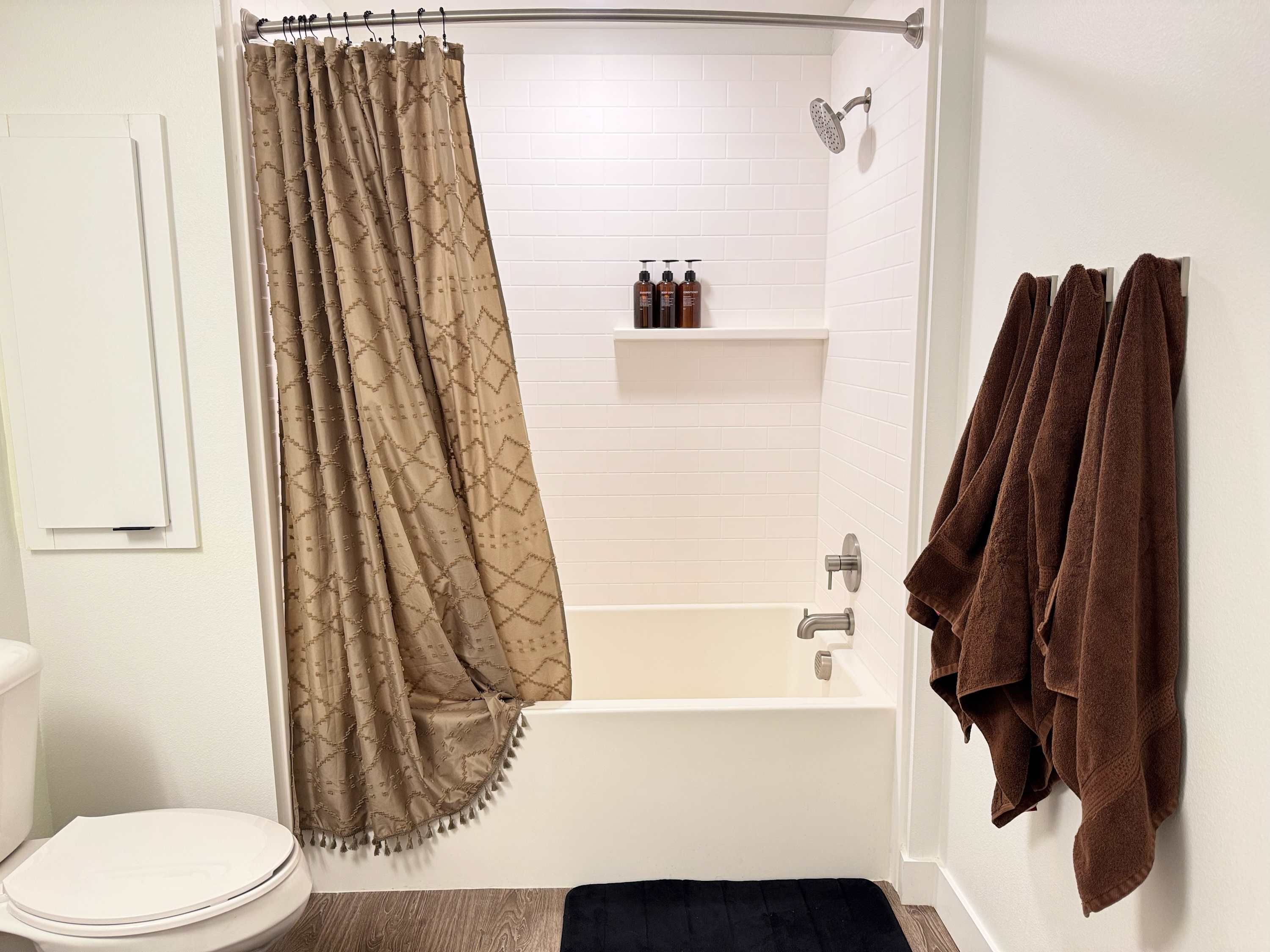 A bathroom with a bathtub, shower, toilet, and a towel rack with towels.