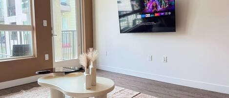 A modern living room with a flat-screen TV mounted on the wall, a small round table, a bench, and a decorative vase with pampas grass.