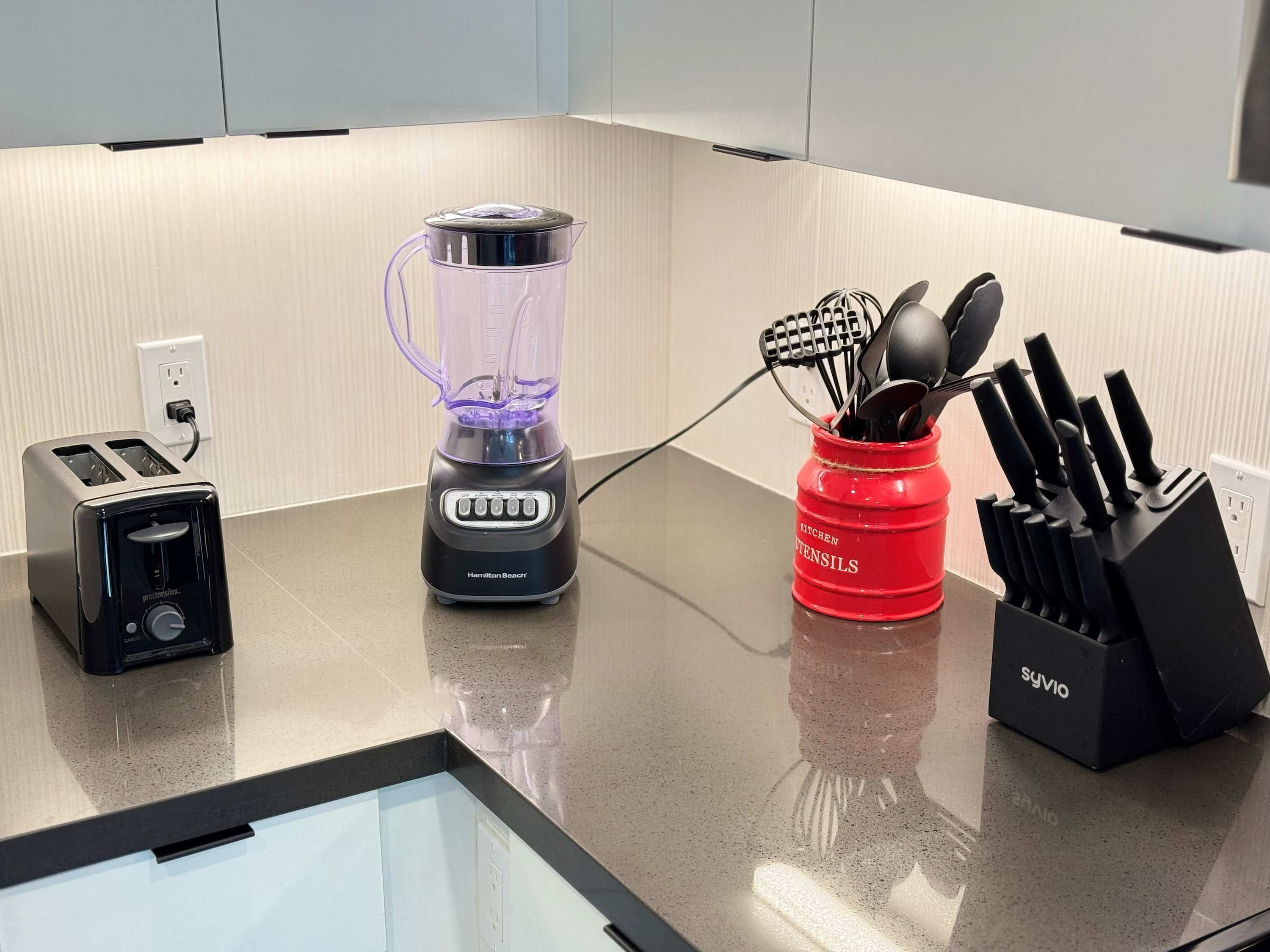 A kitchen counter with a toaster, a blender, a red utensil holder, and a knife block.
