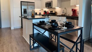 Une cuisine moderne avec des meubles blancs, des appareils en acier inoxydable et une table à manger noire avec des chaises.