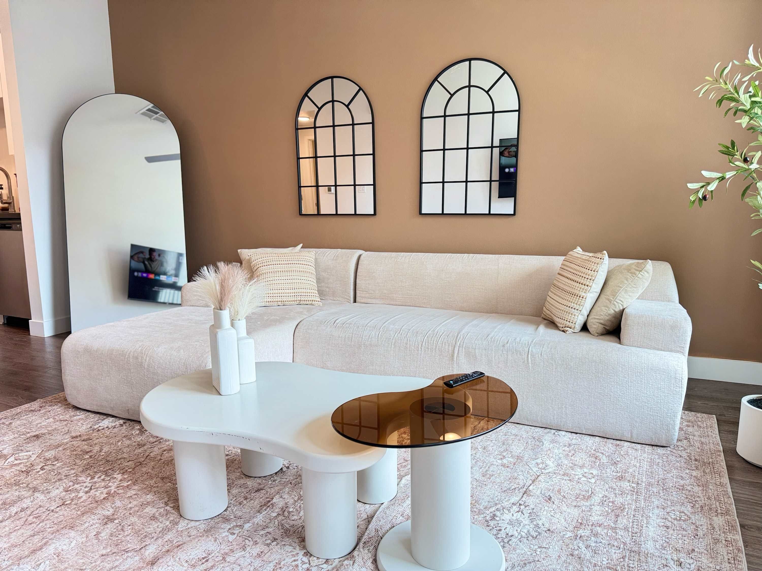 A modern living room with a light-colored sofa, a white coffee table, and a large mirror on the wall.