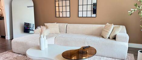A modern living room with a light-colored sofa, a white coffee table, and a large mirror on the wall.
