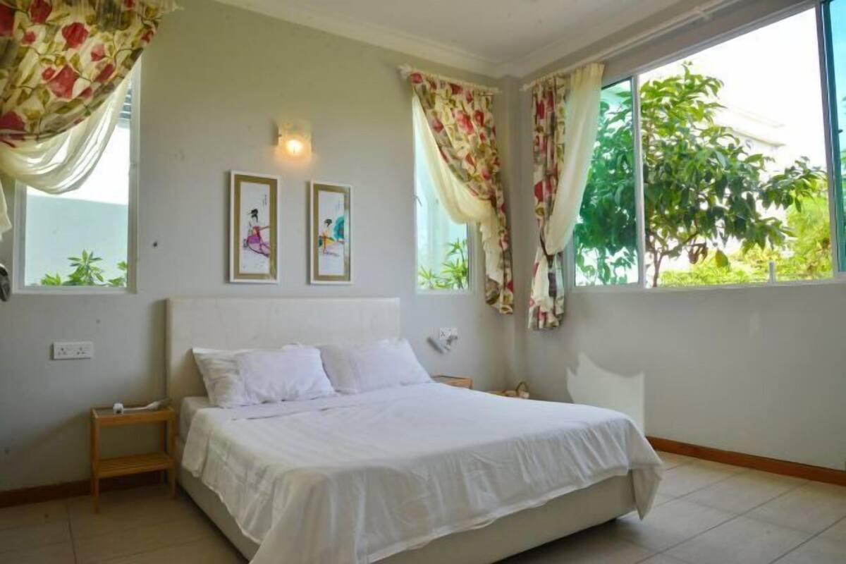 A bedroom with a bed, a nightstand, two wall-mounted light fixtures, and a window with curtains.