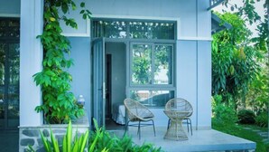 A modern building with a stone base and a glass door leading to a room. There are two wicker chairs outside on a patio with a view of greenery. - MyGarden Villa Binh Chau Hotspring (Binh Chau)