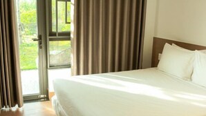 A hotel room with a bed, curtains, and a view of greenery outside. - MyGarden Villa Binh Chau Hotspring (Binh Chau)