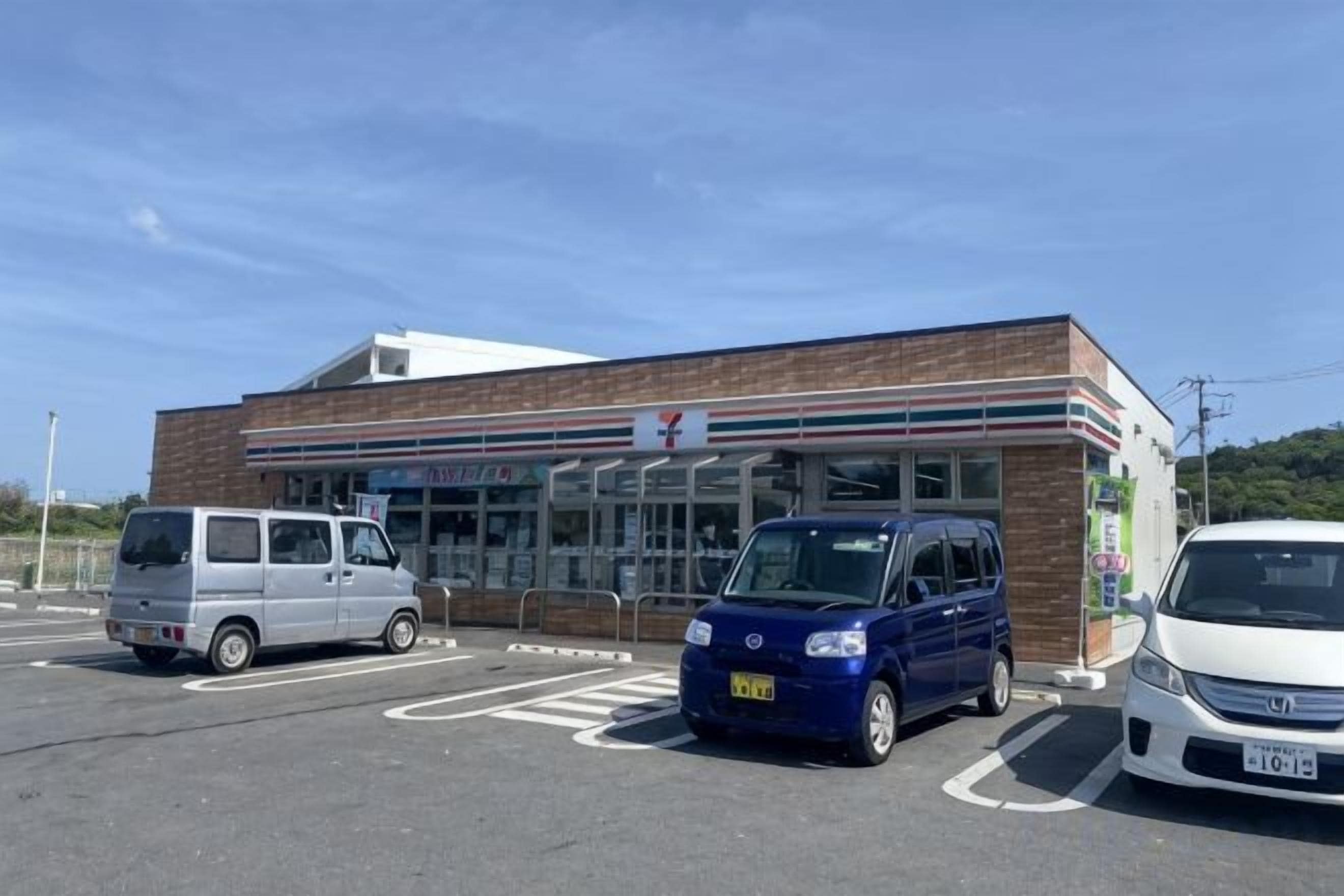 Ein 7-Eleven-Kiosk mit Parkplatz und drei parkenden Autos davor.