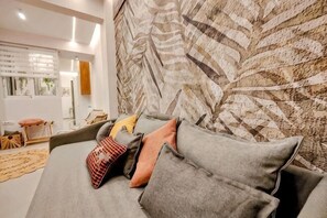 A modern living room with a grey sofa, patterned wall, and a view of the adjacent room. - Elpis' cozy & luxury apartment (West Athens)
