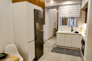 A compact kitchen with a refrigerator, a sink, and a window with blinds. - Elpis' cozy & luxury apartment (West Athens)