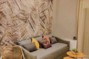Een moderne woonkamer met een bank, kussens, een klein rond tafeltje en een decoratieve wand.