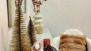 A white sofa with a brown furry throw pillow, a small pink candle, and a pine cone on a white table.