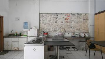 A classroom with a bulletin board, a desk, a chair, and a refrigerator.
