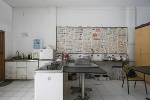 Uma sala de aula com um quadro de avisos, uma mesa, uma cadeira e um frigorífico.