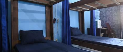 A room with two beds, wooden beams, a window with curtains, and a mirror on the wall.
