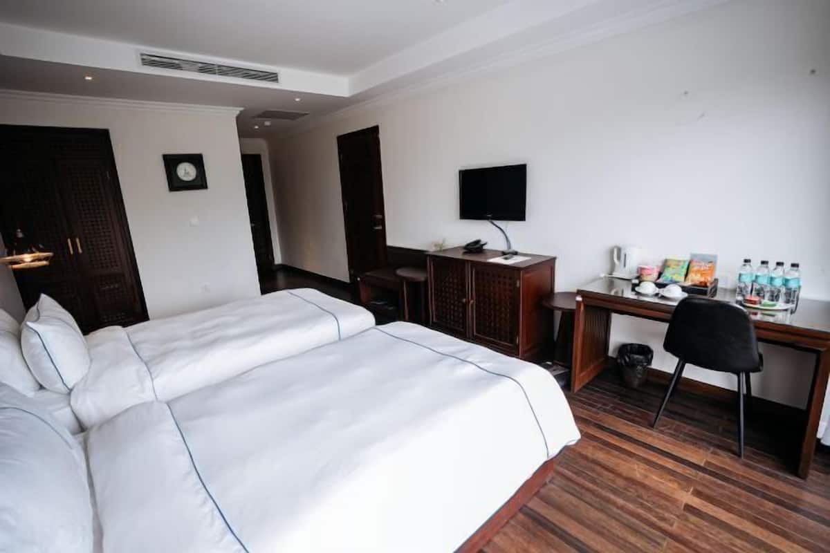 A hotel room with a large bed, a desk with a computer, a TV, and a small table with drinks.
