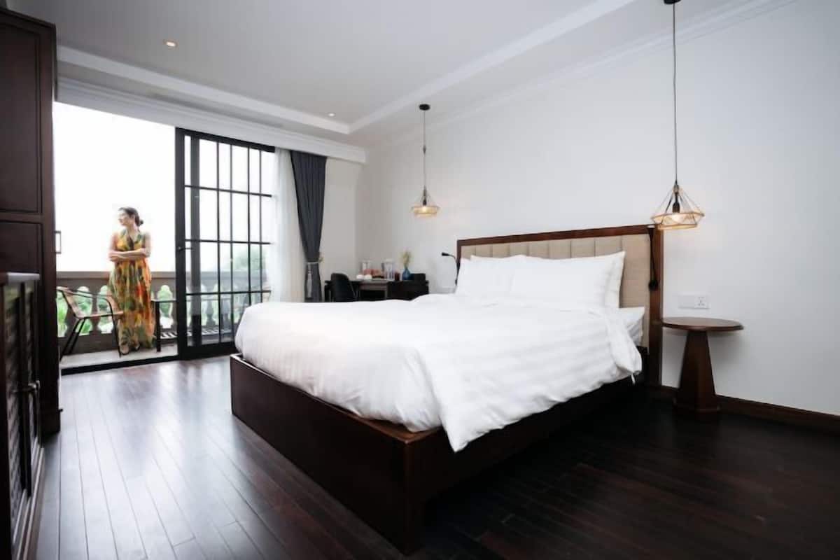 A spacious bedroom with a large bed, a small bedside table, a nightstand, and a view of a balcony.