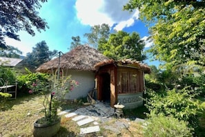 A rustic house with a thatched roof, surrounded by lush greenery and a stone pathway leading to the entrance. - Paradise Soc Son Resort (Hanoi)