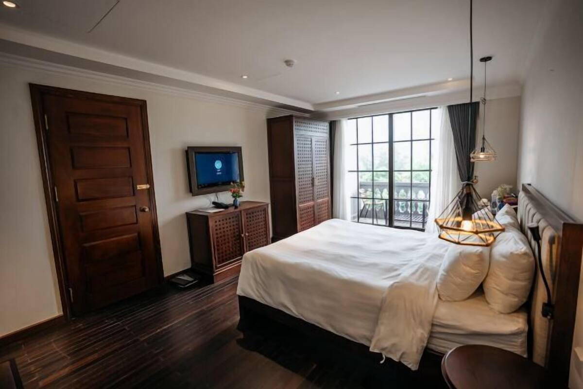 A hotel room with a large bed, a television, a wooden cabinet, and a window with a view.