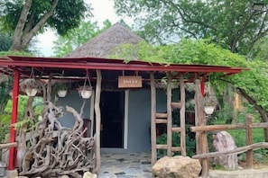 A rustic building with a thatched roof, a wooden sign, and hanging planters.